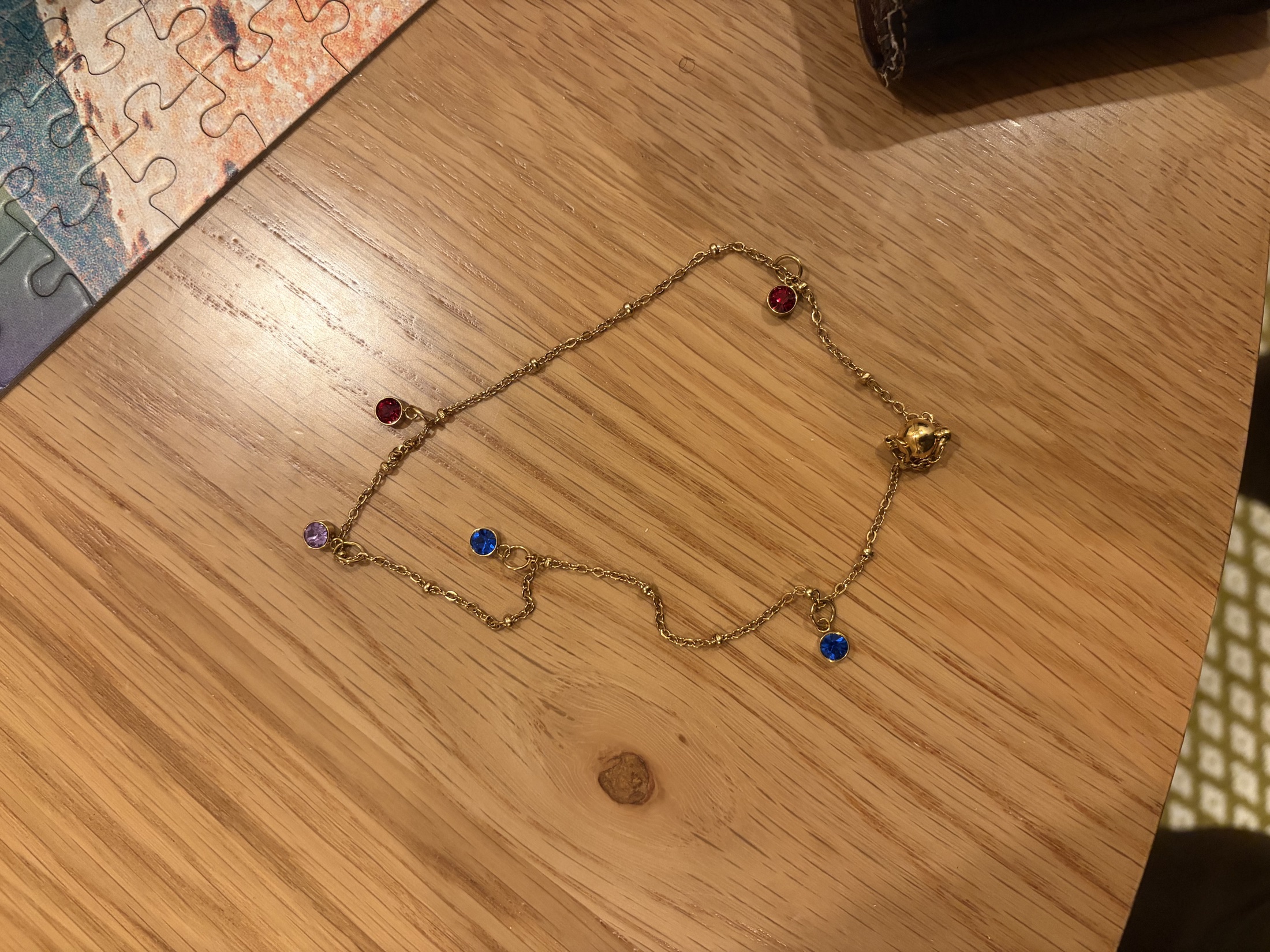 A fine gold bracelet with blue, violet, and red stones arranged on a wooden table.