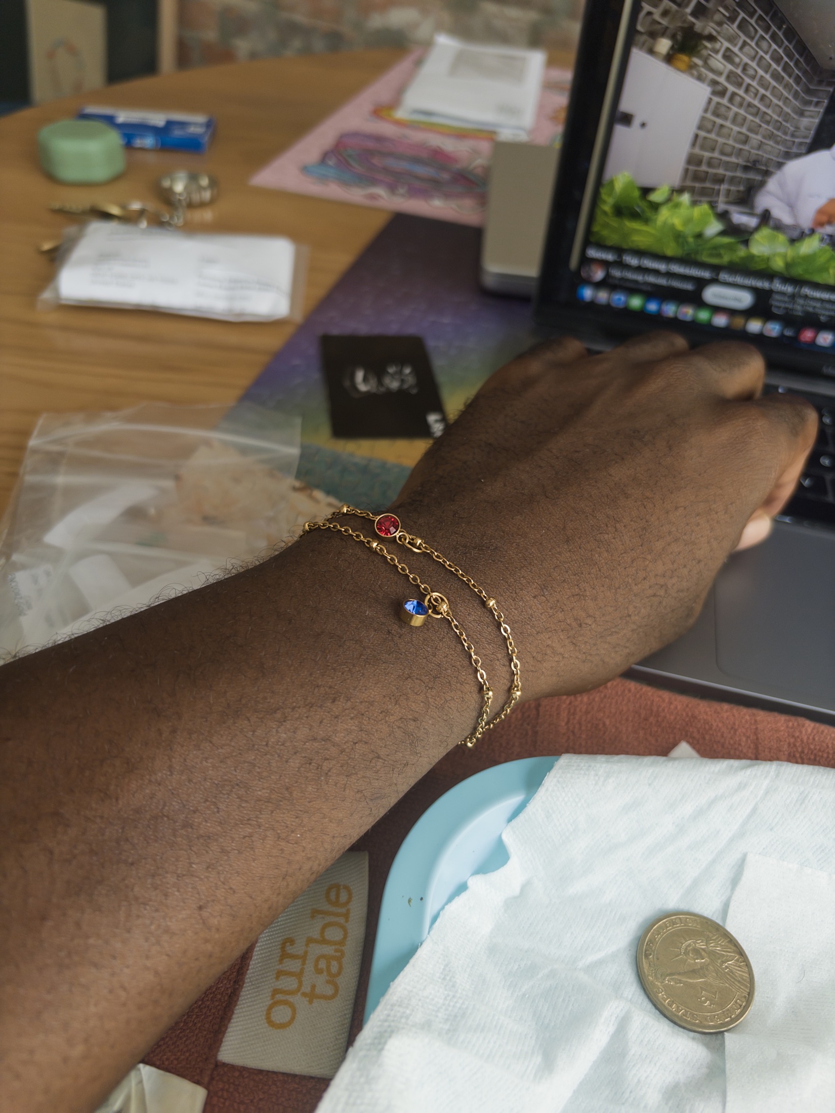 A gold charm bracelet with colourful stones worn on a wrist.