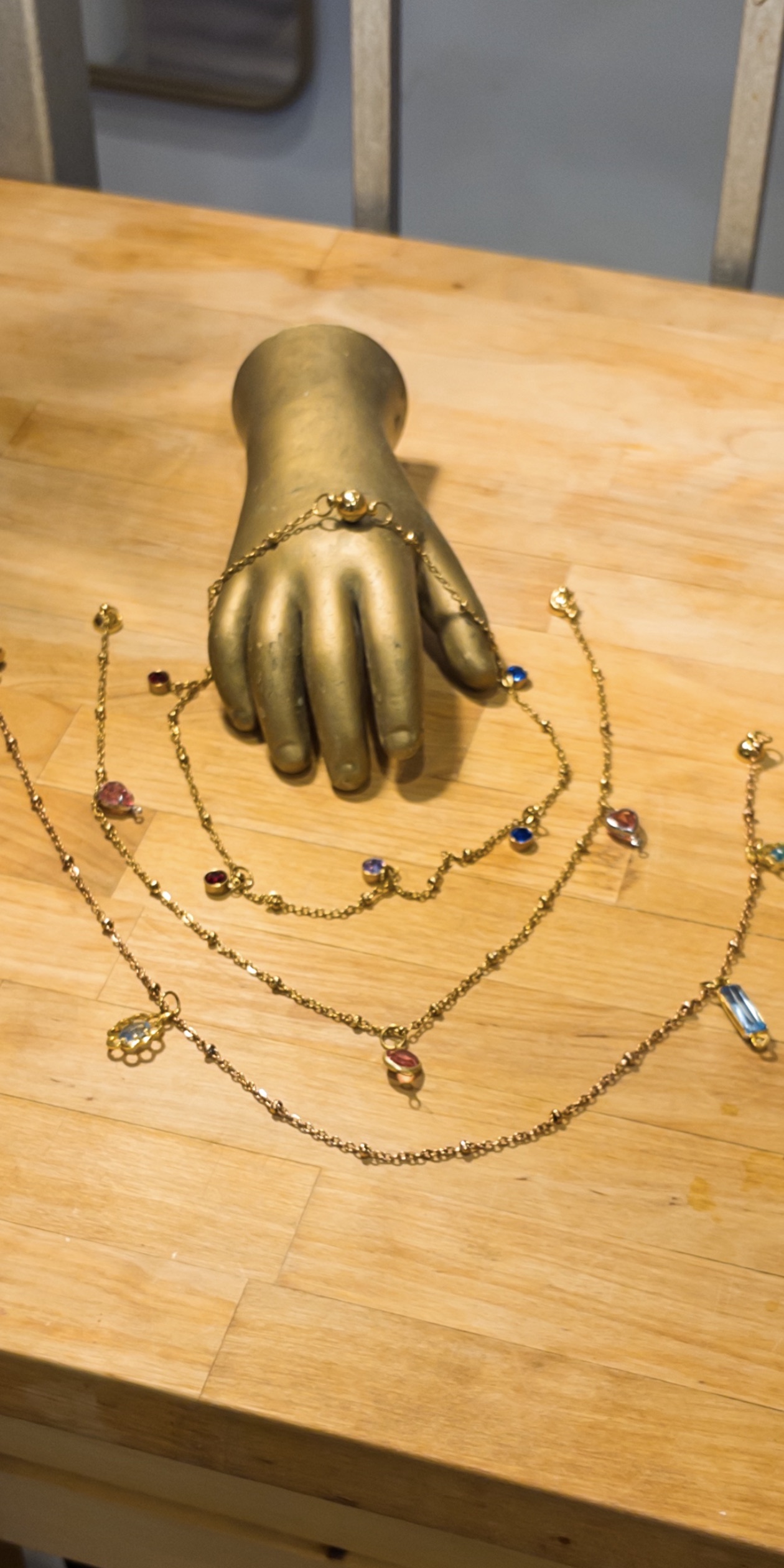 A gold hand form surrounded by colourful charm bracelets on warm wood.