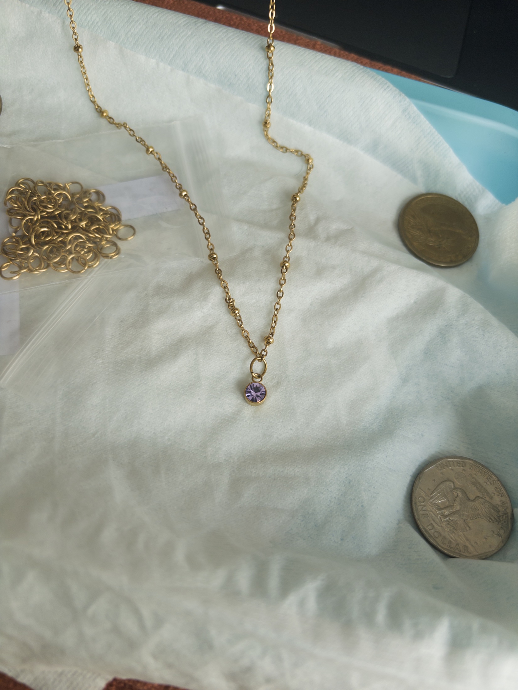 A fine gold bracelet with a violet stone charm on a pale fabric background.